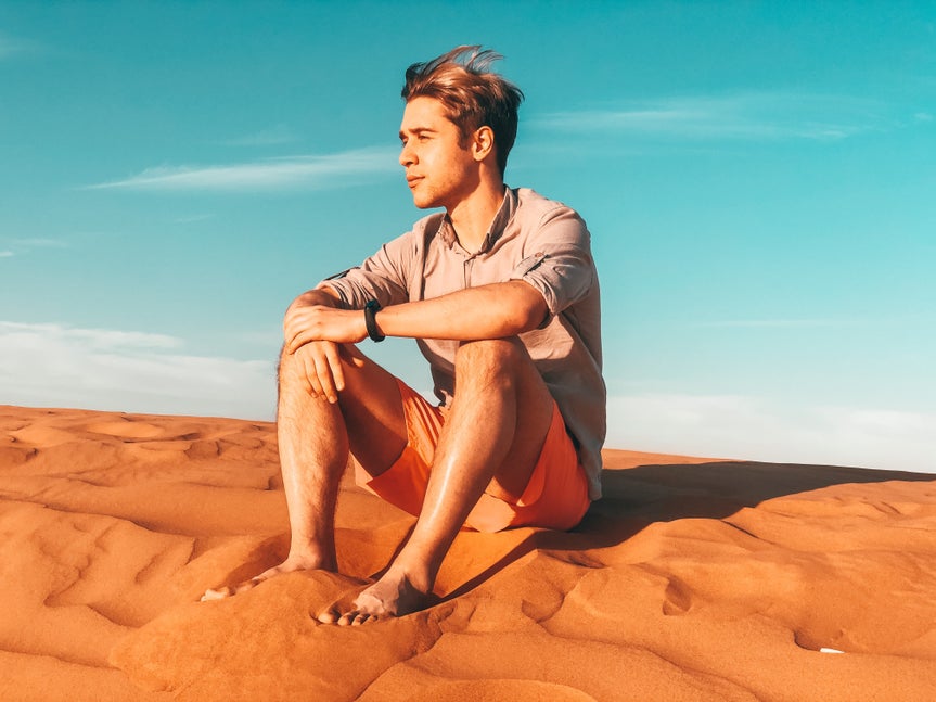 Photo of young man sitting on sand with a blue sky in the background